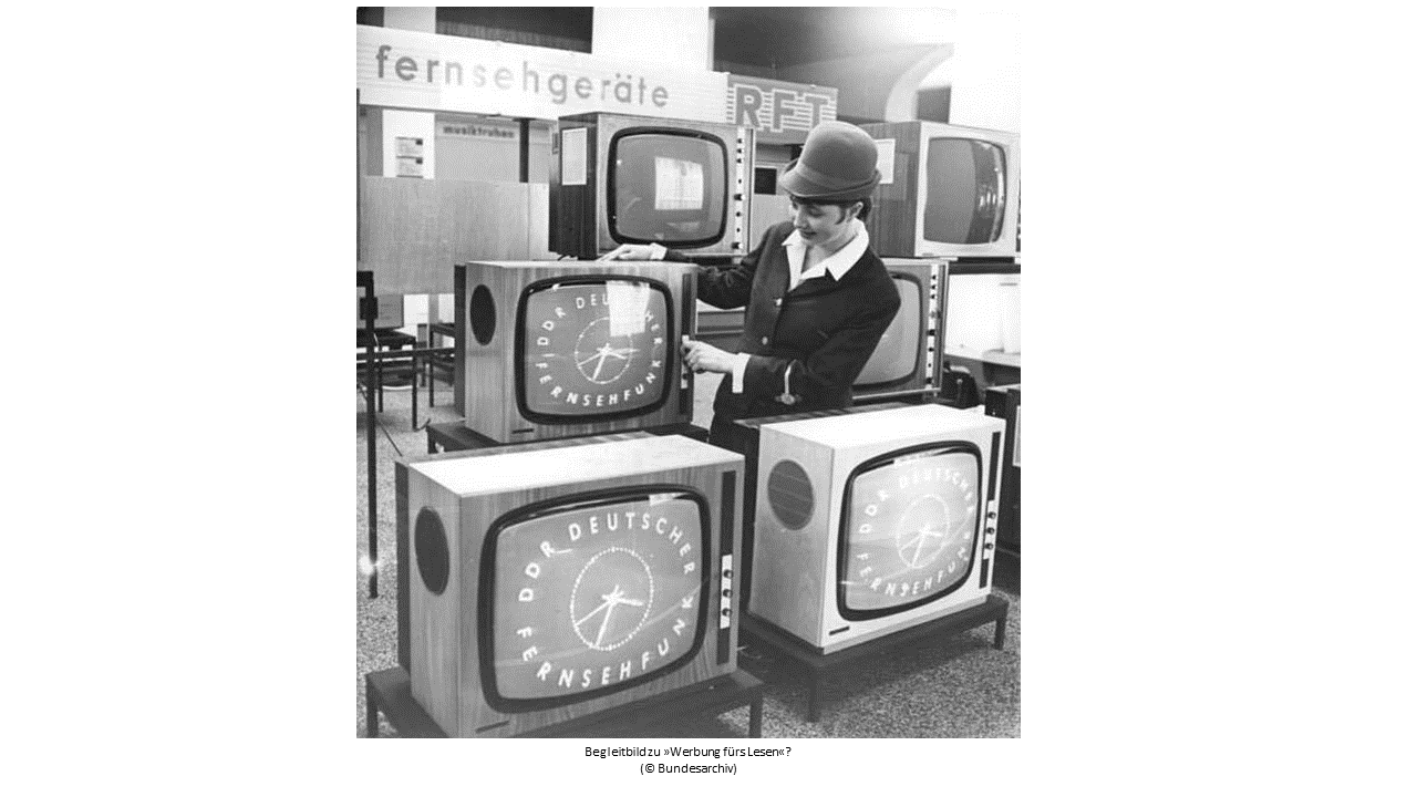 Auf dem Bild zu sehen sind 5 Fernseher, angeordnet wie eine Pyramide, die in einer Kaufhausabteilung für Fernsehgeräte in der DDR von einer jungen Verkäuferin vorgeführt werden. Auf den Bildschirmen der Fernsehgeräte steht: DDR Deutscher Fernsehfunk.